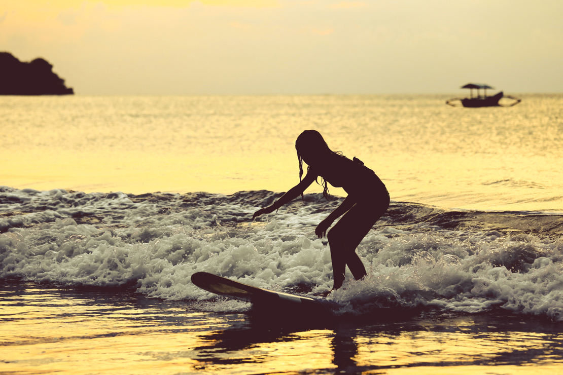 shutterstock_492020038 Silhouette of surfer girl surfing on her board on the tropical Jimbaran beach..jpg